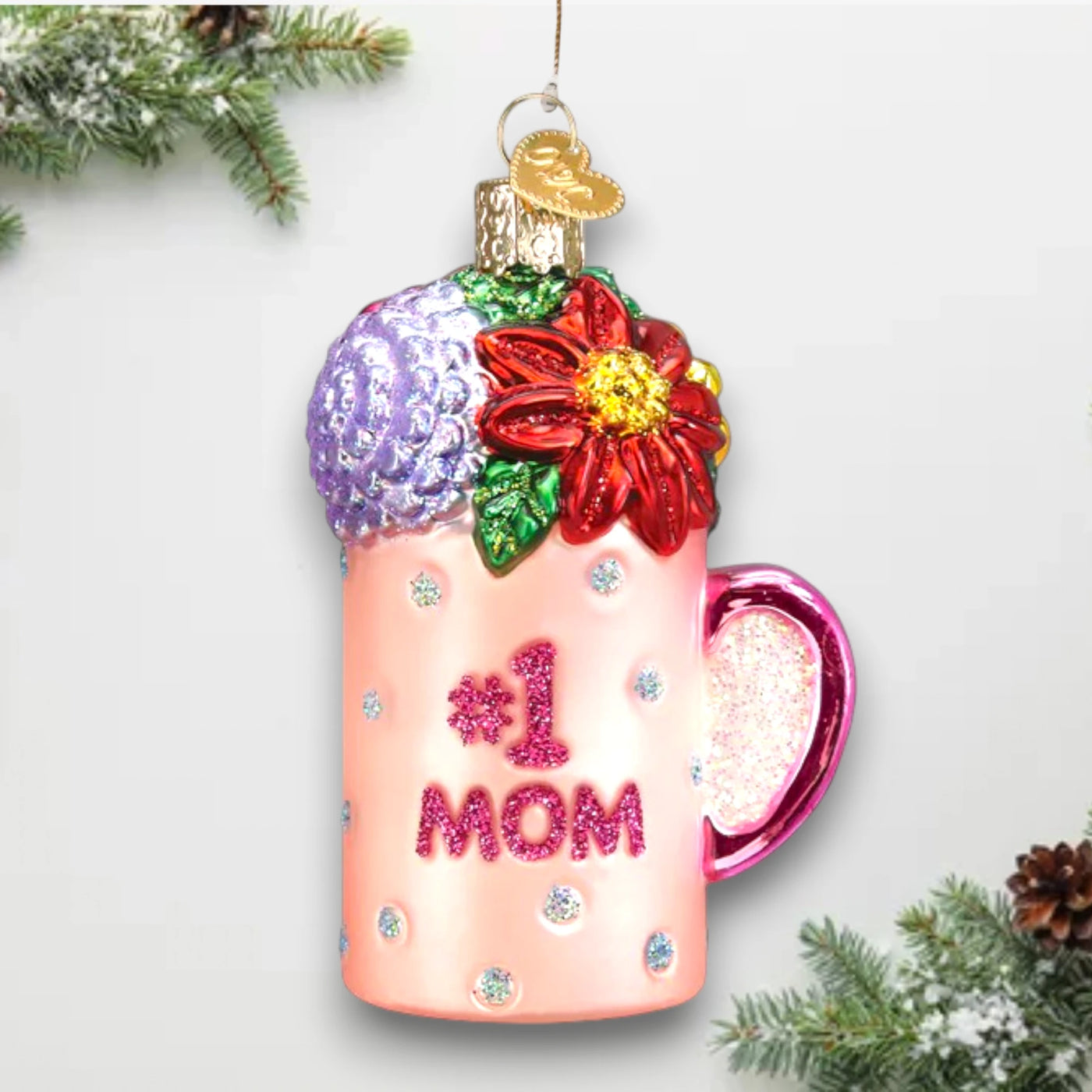 Pink “#1 Mom” mug Christmas ornament with glitter accents and colorful floral decorations, customizable with name and year.