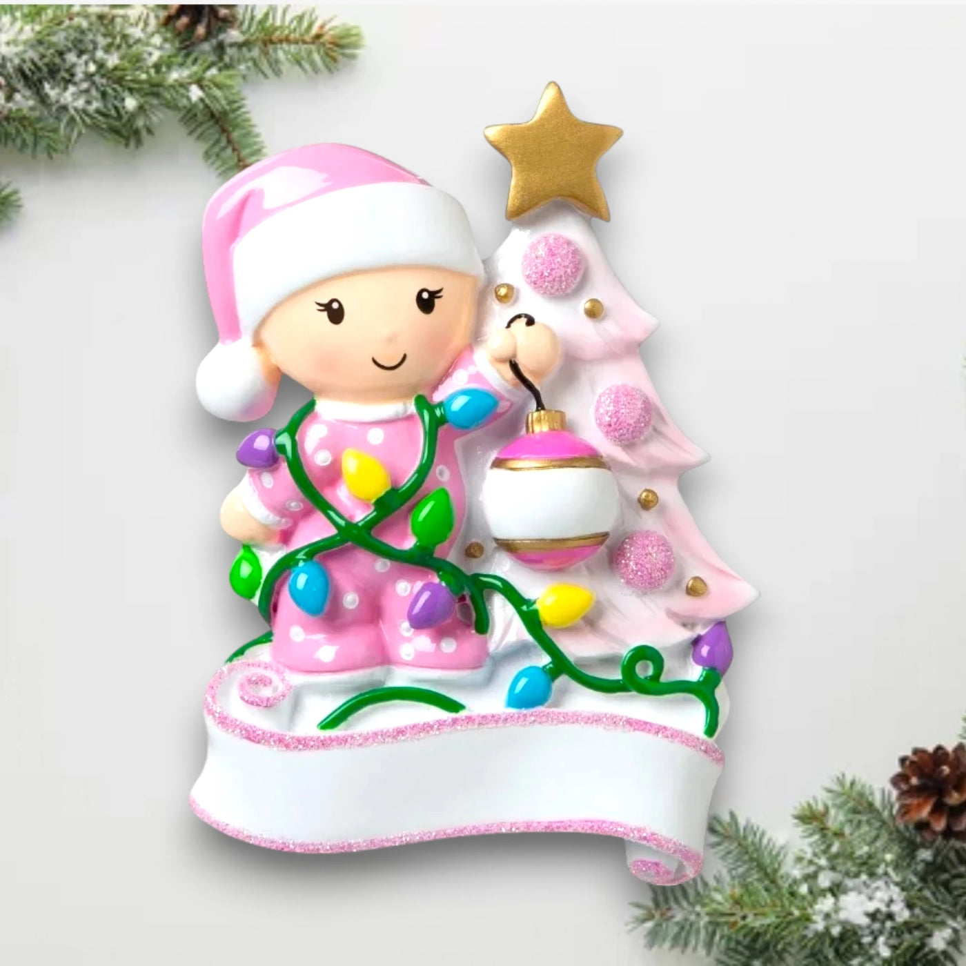 Personalized Baby Decorating A Tree Pink Christmas Ornament with customizable name and year, featuring a baby girl with holiday lights and a decorated Christmas tree.