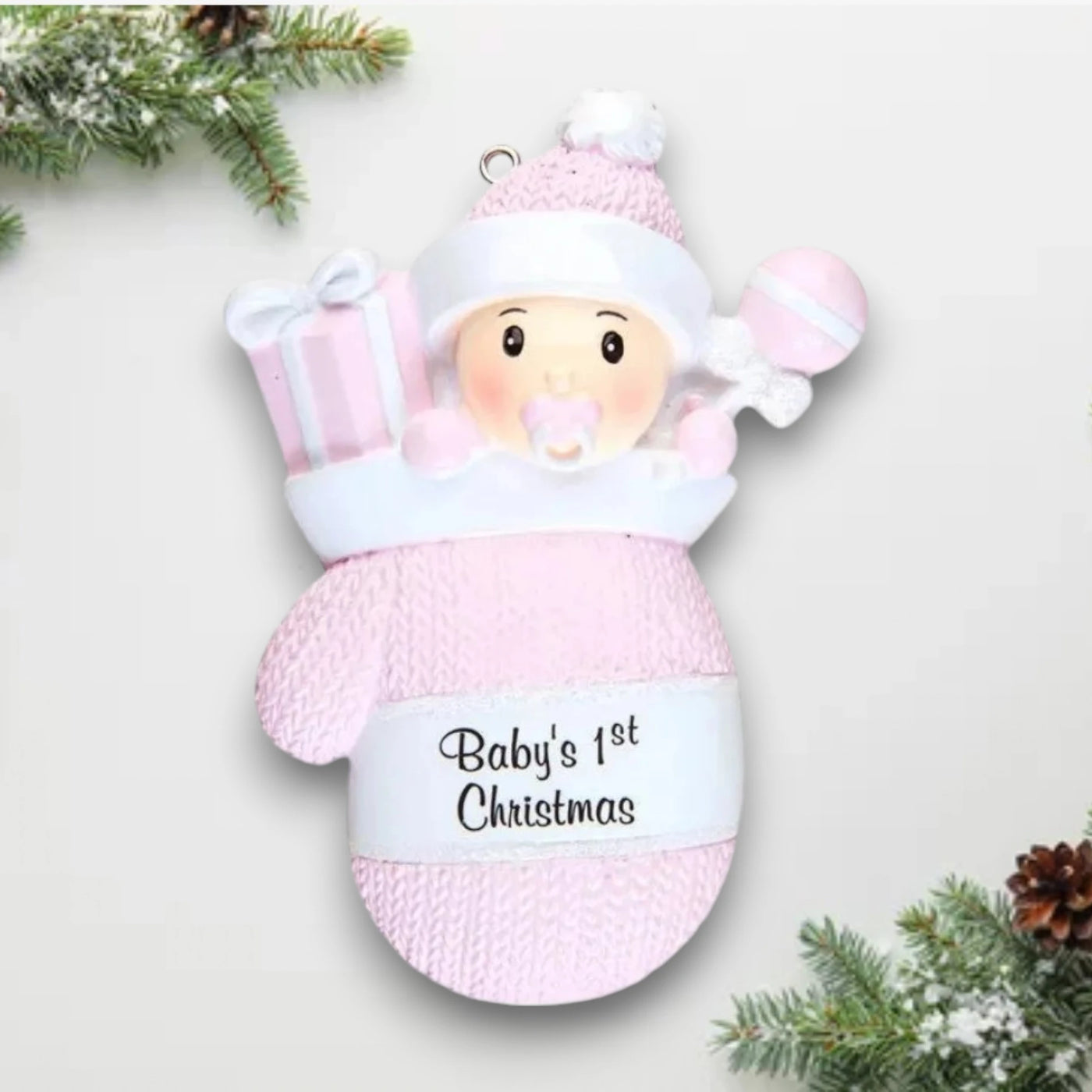 Personalized Baby Girl In Mitten Ornament with pink knit pattern, baby girl in winter hat and pacifier, customizable with name and year.