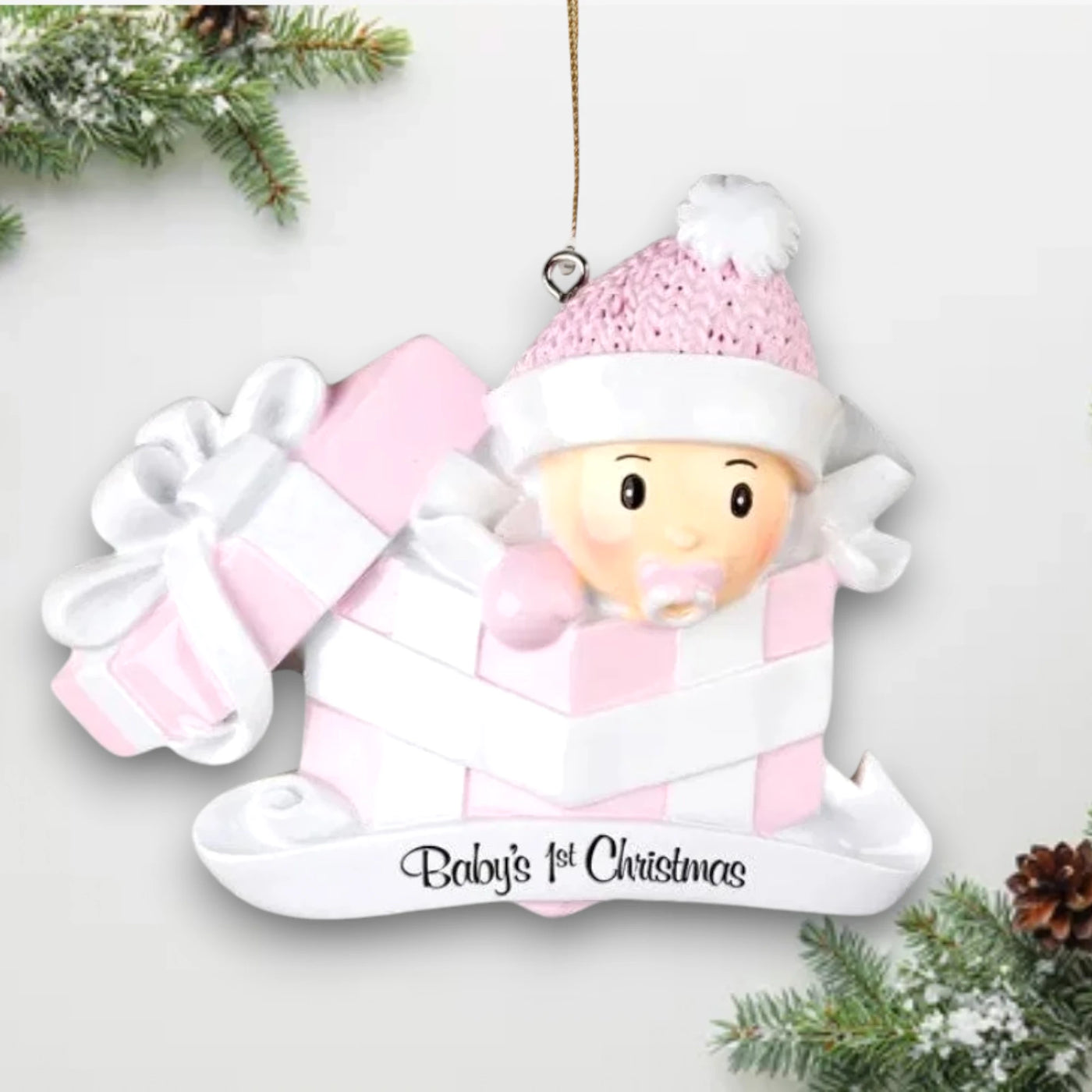 Personalized Baby Girl In Present Ornament with pink knit hat, peeking from a pink and white gift box, customizable with name and year.