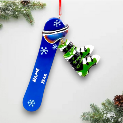 Personalized Snowboard Christmas Ornament featuring a blue snowboard with white snowflake details and dangling green snowboard boots, customizable with name and year.

