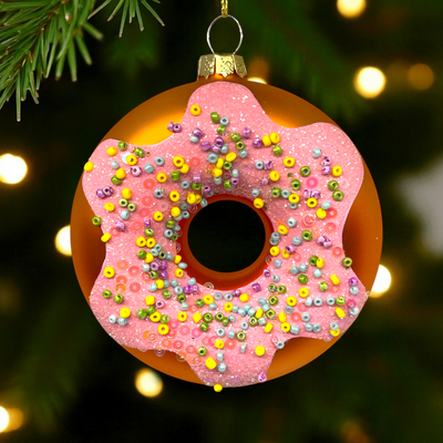 Decorative pink donut ornament with colorful sprinkles on a Christmas tree.