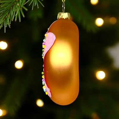 Decorative Christmas ornament shaped like a gold candy bar with pink top, hanging on a tree.