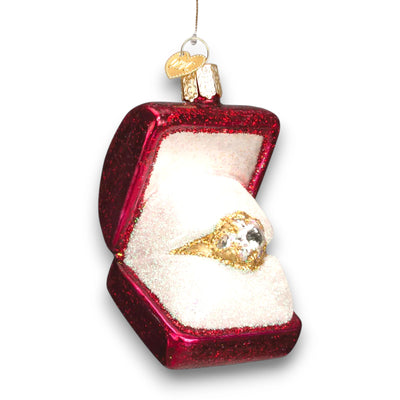 Christmas ornament featuring a glittering gold ring in a red jewelry box with shimmering details, symbolizing love and celebration.