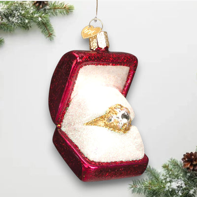 Christmas ornament featuring a glittering gold ring in a red jewelry box with shimmering details, symbolizing love and celebration.